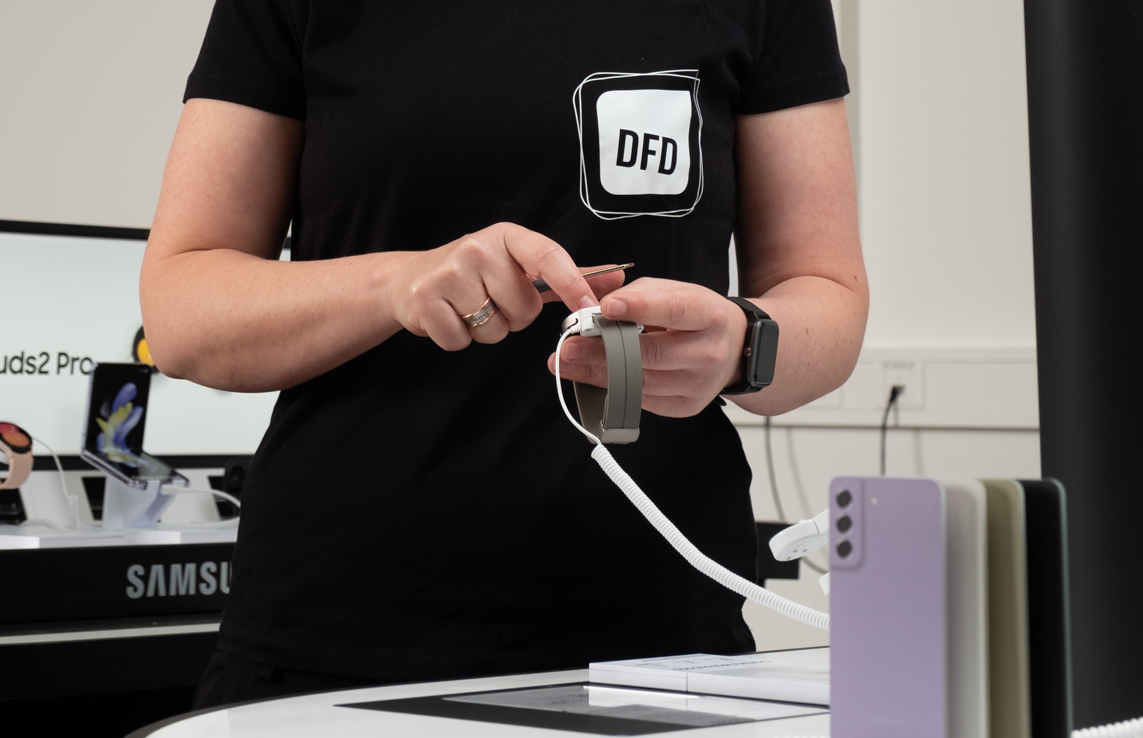 Mitarbeiterin von DFD präsentiert eine Smartwatch in einem modernen Retail-Umfeld.  DFD vereint Kompetenzen für das Retailgeschäft der Zukunft.