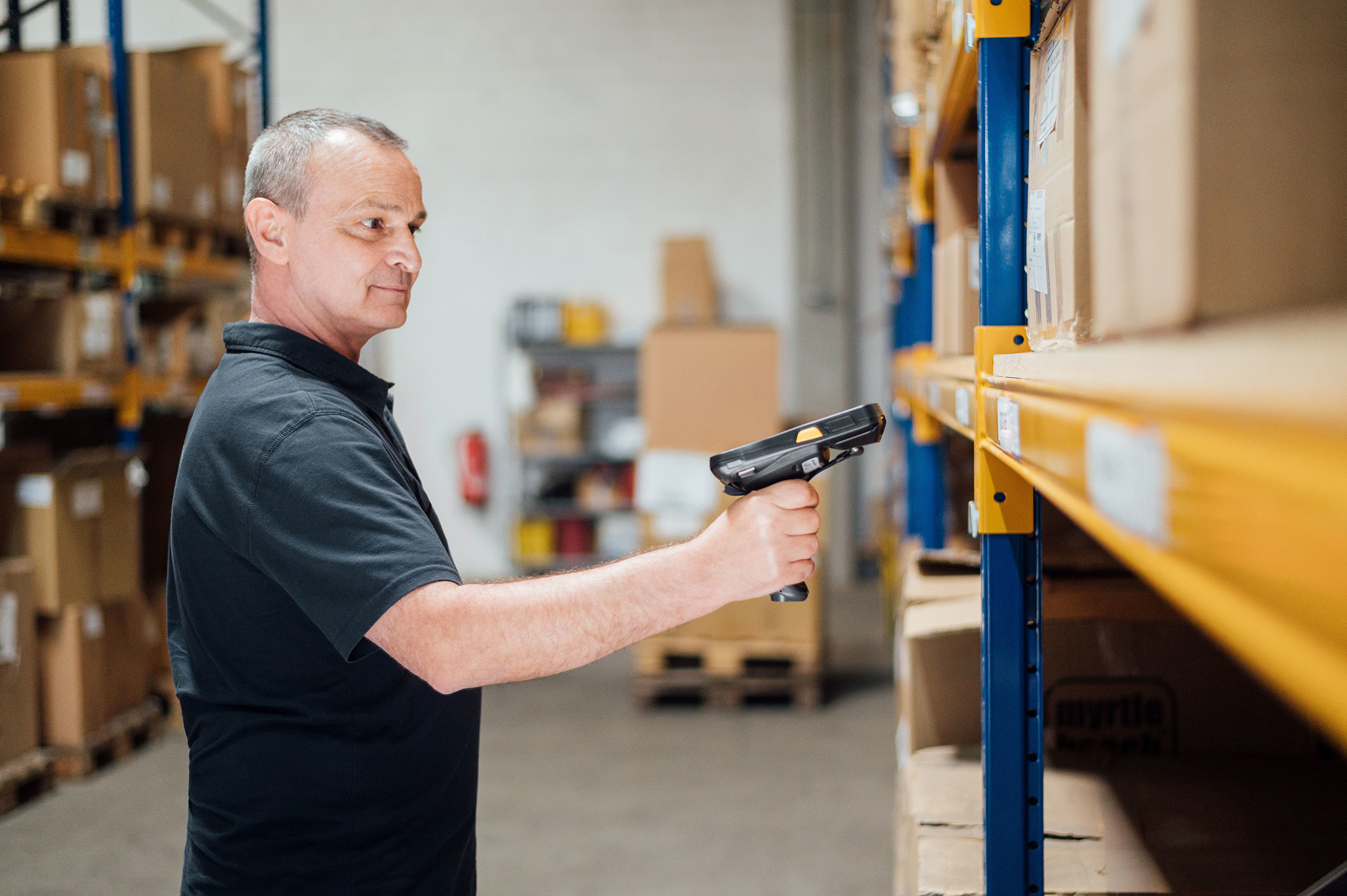 Mitarbeiter scannt Waren in einem Lager, um die Omnichannel-Verknüpfung zu optimieren.  Das Bild zeigt die effiziente Logistik für das Retailgeschäft der Zukunft.
