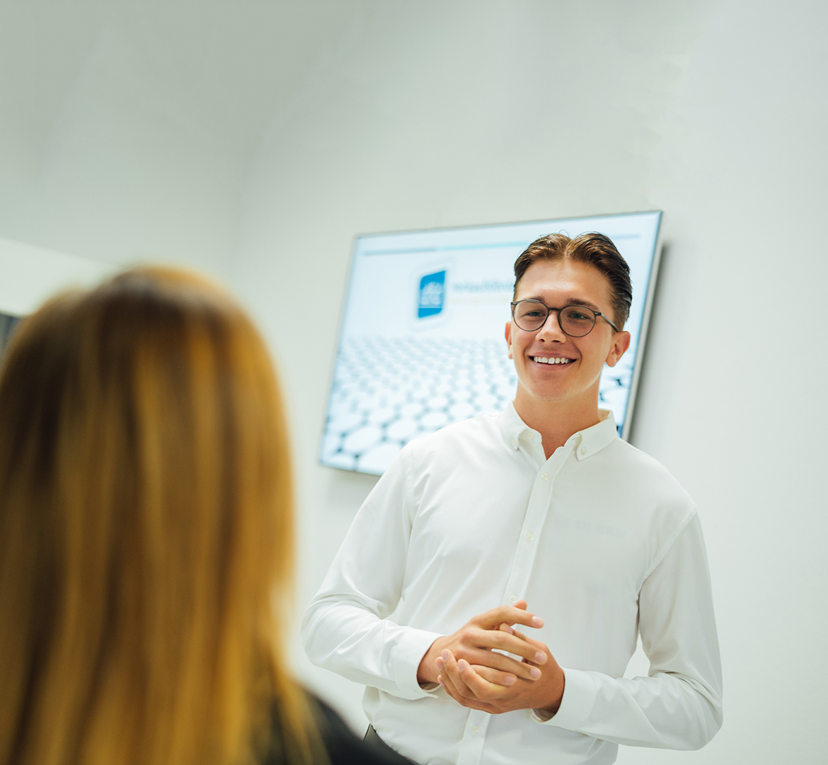 Junger Mann hält Präsentation im Büro, im Hintergrund ein Bildschirm mit Firmenlogo. Ein Mitarbeiter von [Firmenname] erklärt die Omnichannel-Strategie.