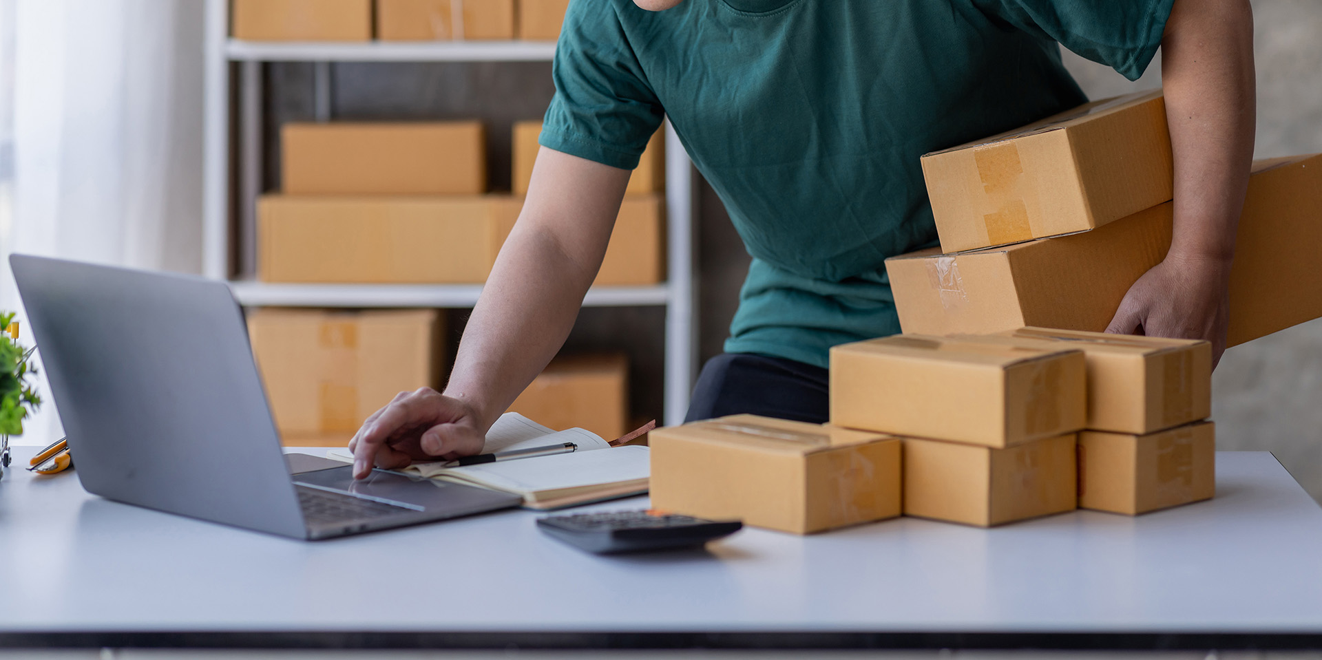 Person arbeitet im Büro mit Laptop und Paketen, um das Retailgeschäft der Zukunft zu gestalten. Versand und Omnichannel-Verknüpfung für mehr Kundennutzen.