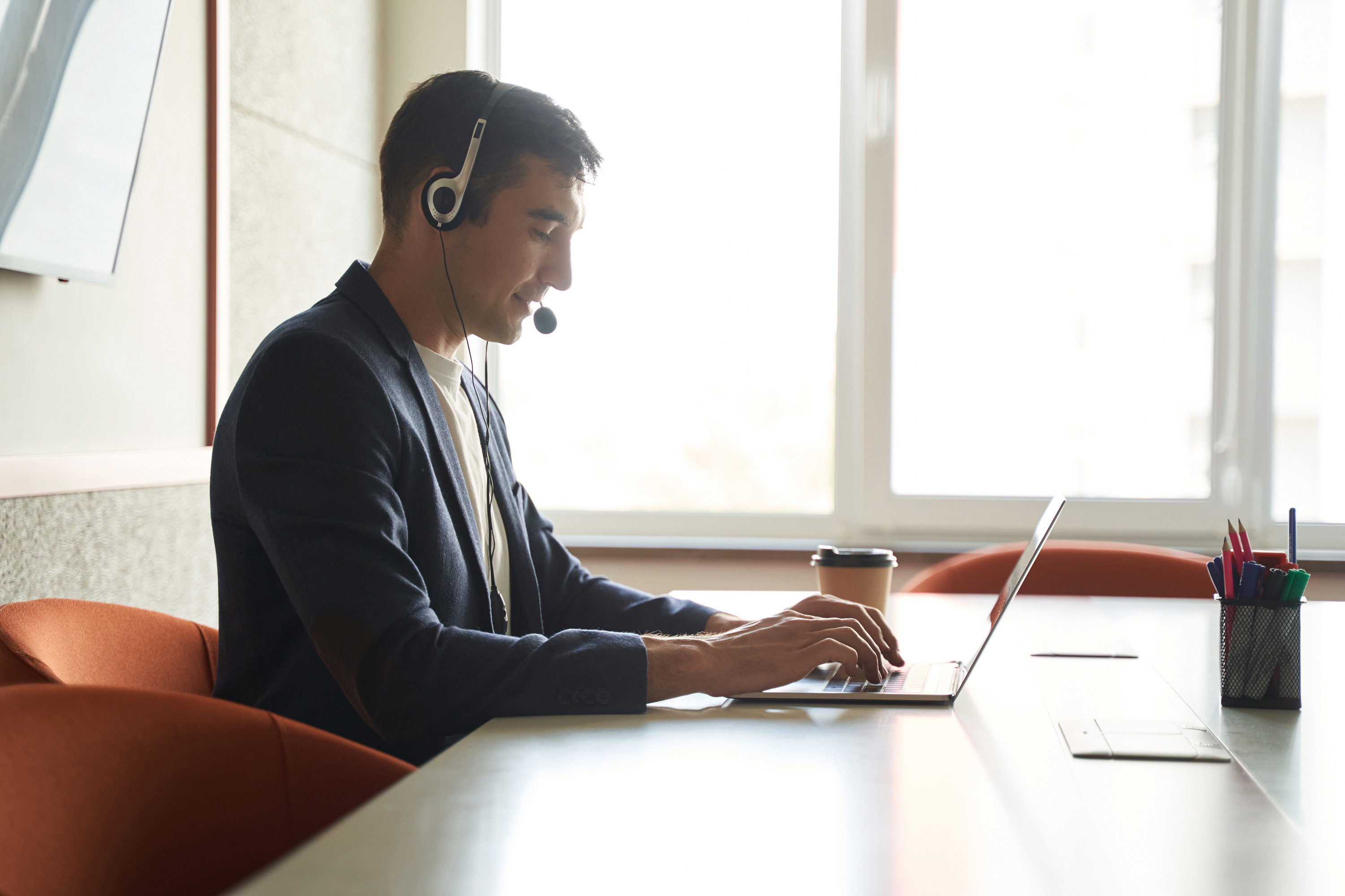 Mann im Büro mit Headset, der an einem Laptop arbeitet.  Ein Mitarbeiter, der für die Zukunft des Einzelhandels arbeitet.