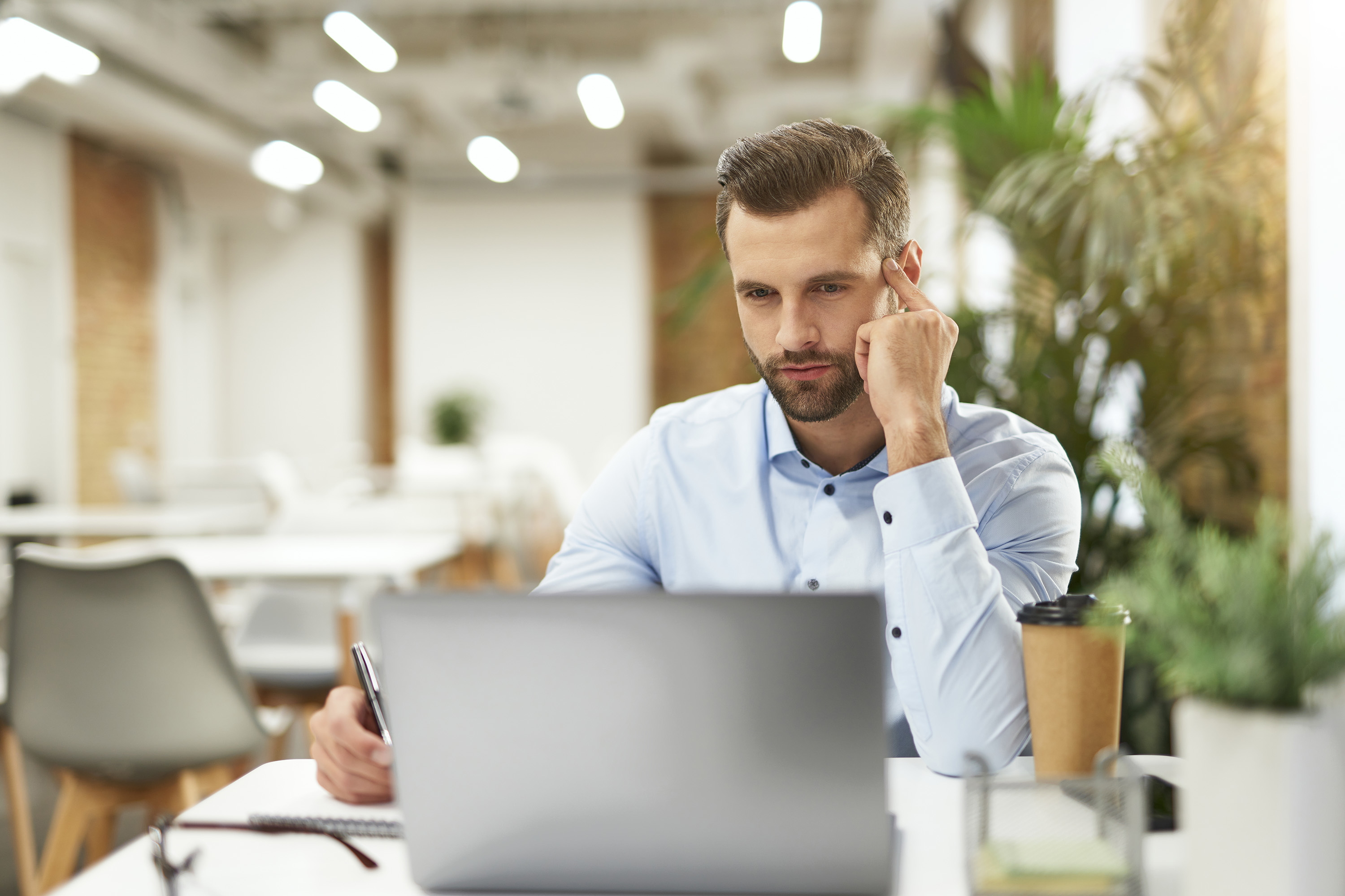 Mann im Büro arbeitet konzentriert am Laptop, um das Retailgeschäft der Zukunft zu gestalten. Der Mann denkt über die Omnichannel-Verknüpfung nach.