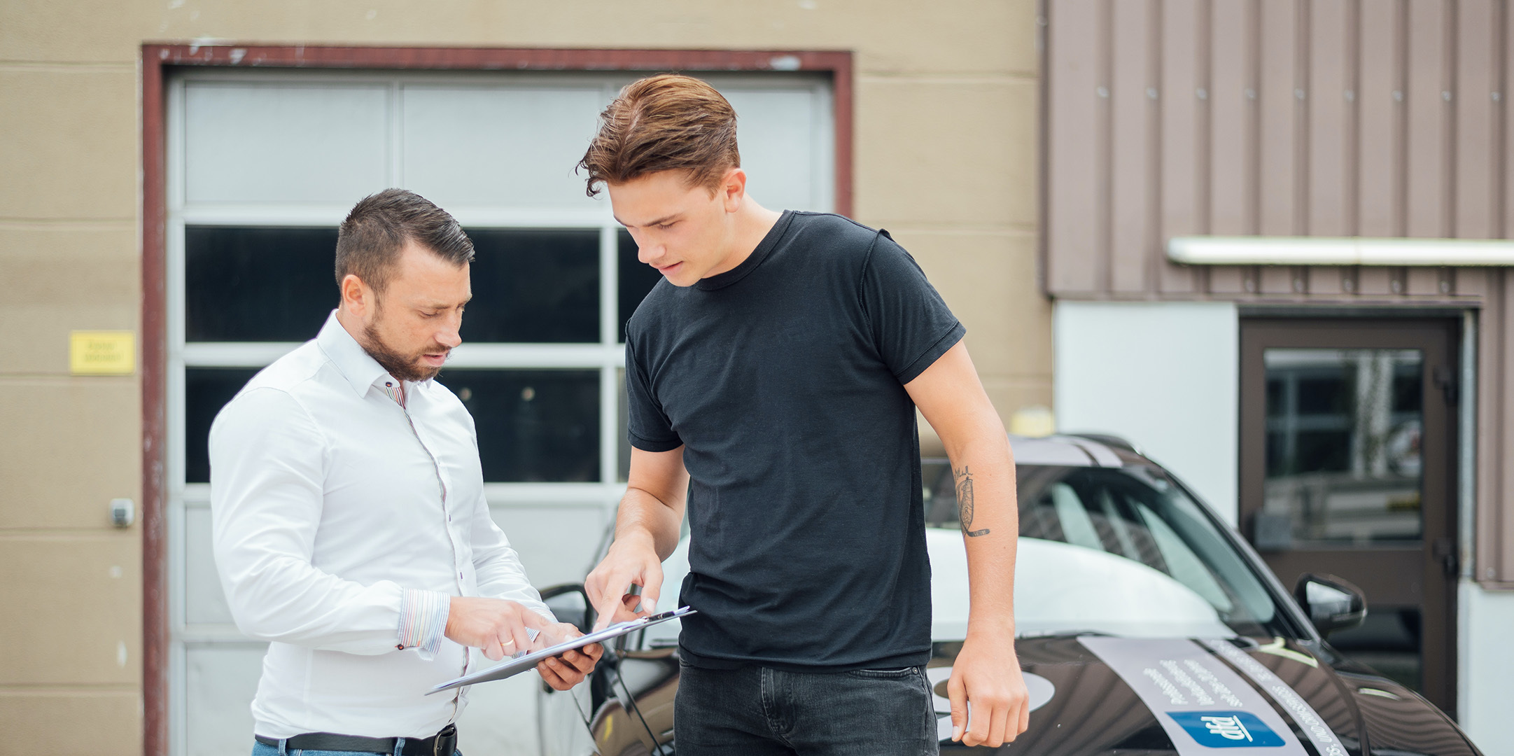 Zwei Männer besprechen Dokumente vor einem Auto, ein Beispiel für unsere Omnichannel-Verknüpfung im Retailgeschäft.