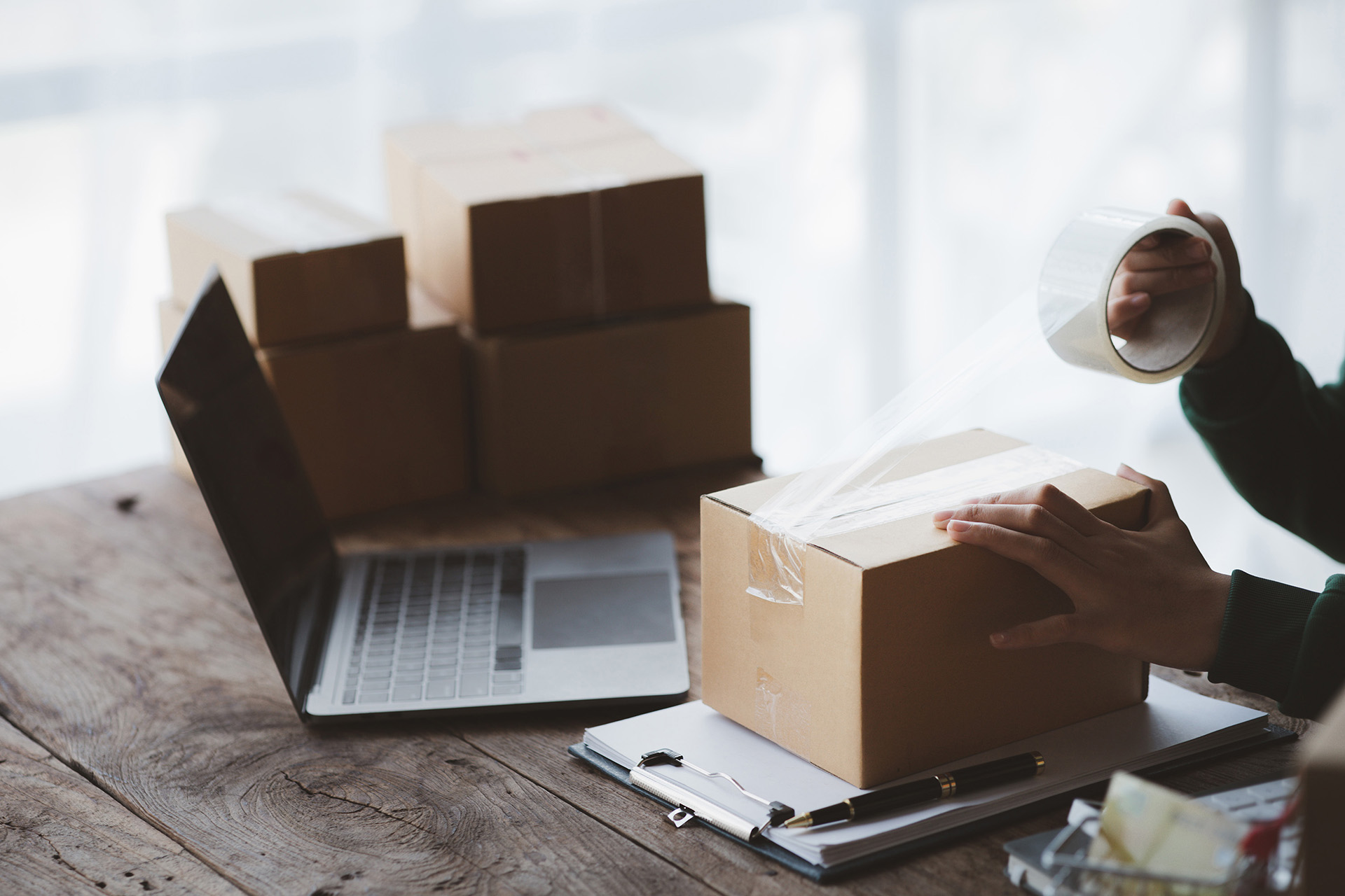 Pakete werden für den Versand vorbereitet, mit Laptop und Klebeband.  Die Omnichannel-Verknüpfung für den Einzelhandel der Zukunft.