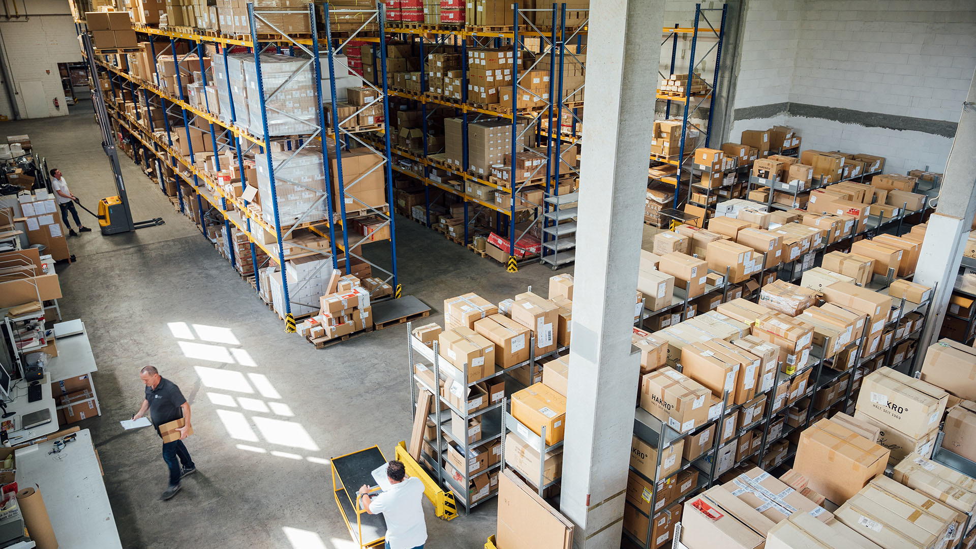 Lagerhalle mit Mitarbeitern und Waren in Kartons, bereit für den Omnichannel-Versand.  Effiziente Logistik für das Retailgeschäft der Zukunft.