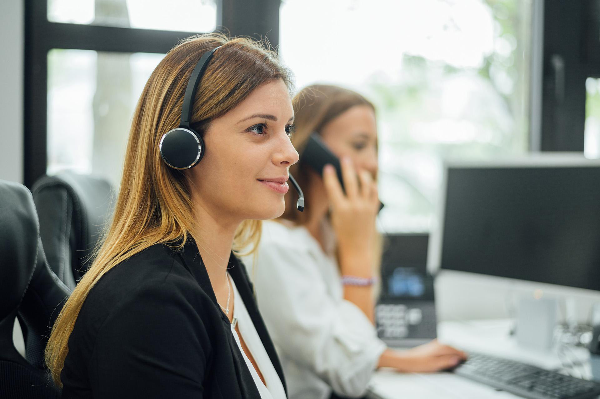 Mitarbeiterinnen im Kundenservice mit Headsets im Büro.  Teammitglieder arbeiten an Computern und Telefonen.